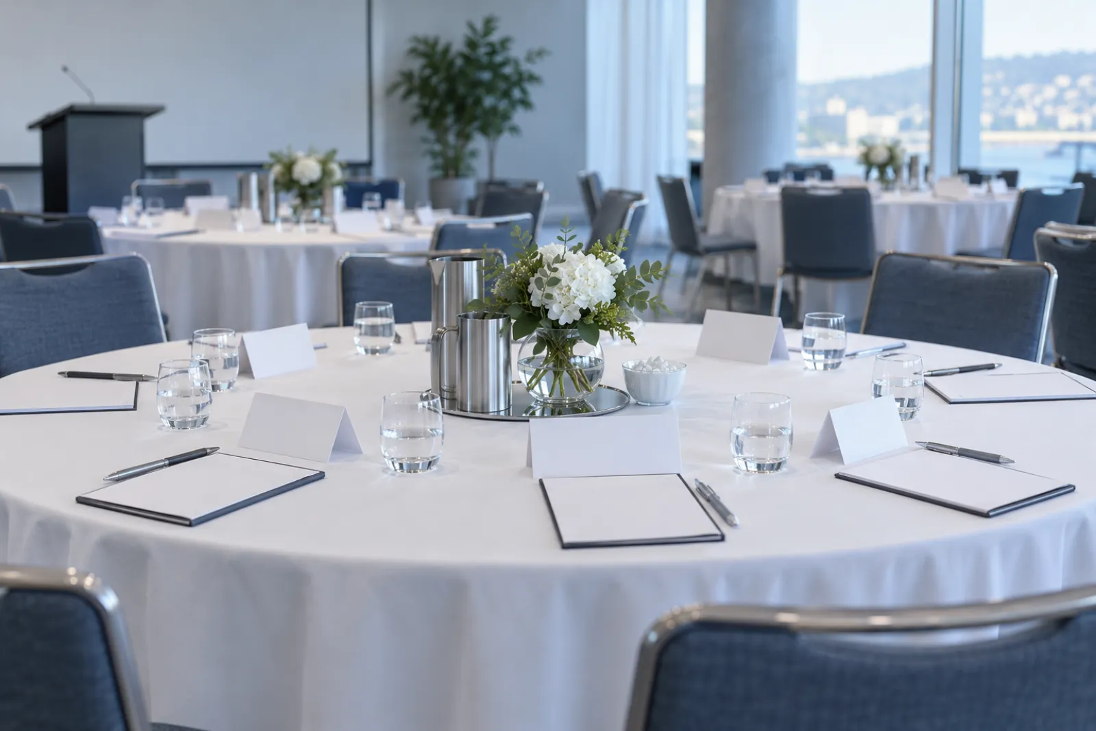 A breakout room set for roundtable discussions: round tables with white cloths, blank name-tent cards, notepads and water glasses, no people